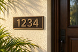 Cast bronze address plaque reading 1234 mounted on a cream stucco wall beside a dark wooden front door