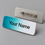 Full-color sublimated aluminum name badge fading from teal to white with Your Name in black, beside a second badge showing a pin-back clasp